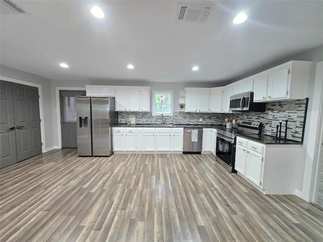 507 W 1st St, Flatonia, TX 78941 - kitchen featuring appliances with stainless steel finishes, dark countertops, backsplash, light wood-style flooring, and white cabinets