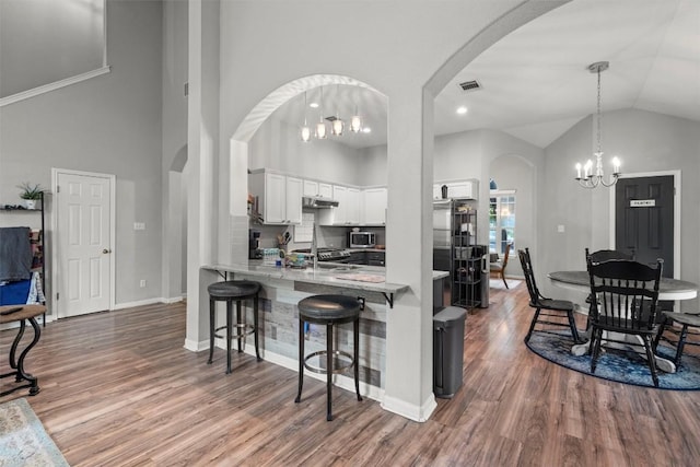 2319 Rock Ledge Dr, Georgetown, TX 78626 - kitchen featuring arched walkways, a chandelier, white cabinets, a breakfast bar, and high vaulted ceiling