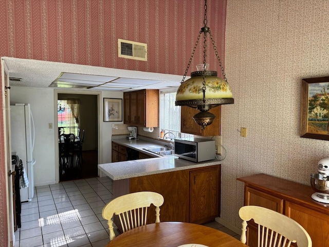 11202 Balcones Woods Cv, Austin, TX 78759 - kitchen with stainless steel microwave, light tile patterned floors, brown cabinets, and wallpapered walls