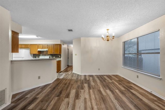 8802 Peppergrass Cv, Austin, TX 78745 - kitchen featuring white refrigerator, under cabinet range hood, a chandelier, dark wood-style flooring, and brown cabinets