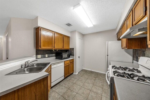 8802 Peppergrass Cv, Austin, TX 78745 - kitchen featuring white appliances, under cabinet range hood, a textured ceiling, brown cabinetry, and tasteful backsplash