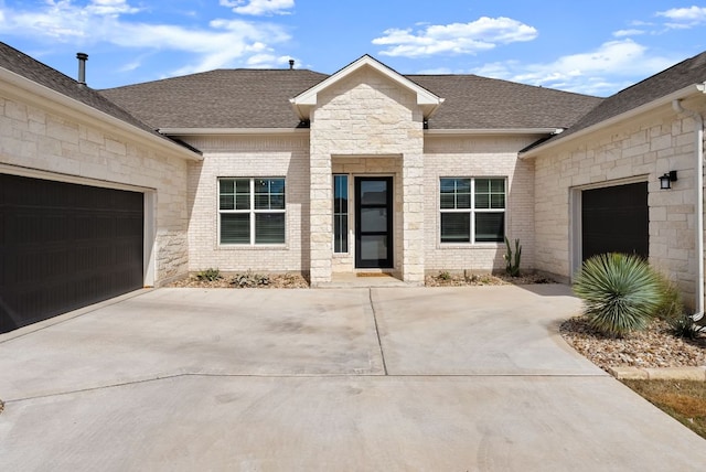 view of front facade featuring a shingled roof, brick siding, a garage, stone siding, and driveway