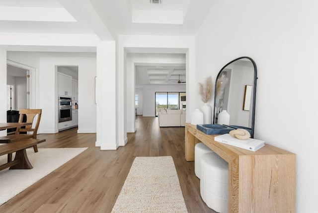 foyer entrance featuring visible vents, beamed ceiling, baseboards, light wood-type flooring, and a raised ceiling