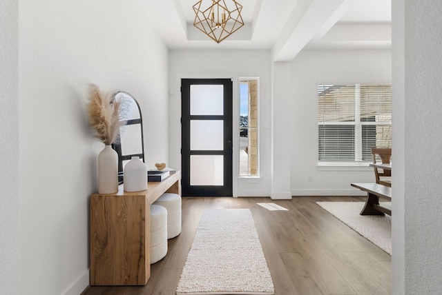 foyer entrance with baseboards, a raised ceiling, wood finished floors, and a chandelier