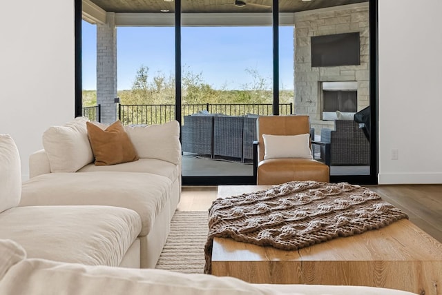 living area with baseboards, floor to ceiling windows, a stone fireplace, and wood finished floors