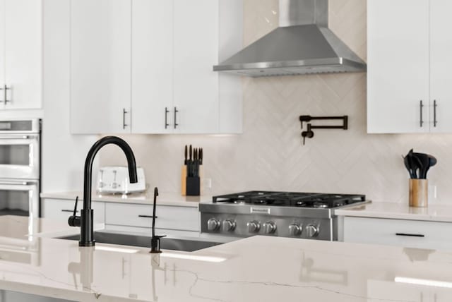 kitchen featuring a sink, decorative backsplash, wall chimney exhaust hood, and white cabinetry