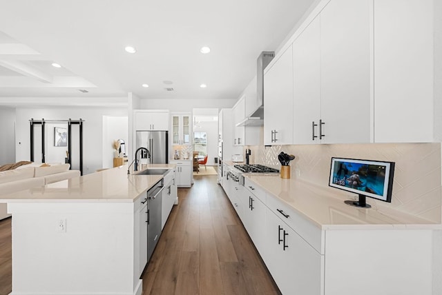 kitchen featuring wood finished floors, recessed lighting, wall chimney exhaust hood, a sink, and stainless steel appliances