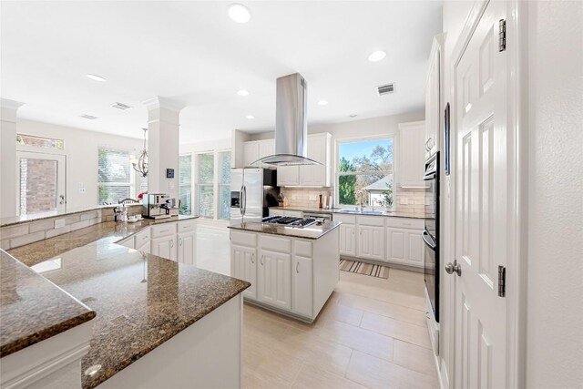 10005 Cormorant Cv, Austin, TX 78730 - kitchen with island exhaust hood, appliances with stainless steel finishes, decorative backsplash, white cabinets, and dark stone countertops