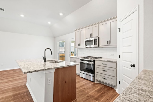 341 Fawn River Run, Kyle, TX 78640 - kitchen featuring stainless steel appliances, a sink, light wood-style floors, a center island with sink, and decorative backsplash