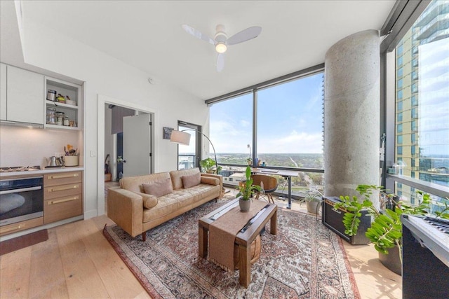 living room with light wood-type flooring, ceiling fan, and a wall of windows