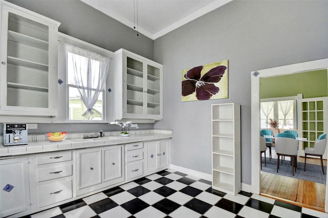 501 Burleson St, Smithville, TX 78957 - kitchen featuring dark floors, tile countertops, white cabinetry, glass insert cabinets, and healthy amount of natural light