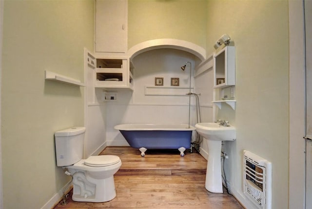 bathroom with a freestanding tub, toilet, baseboards, heating unit, and wood finished floors