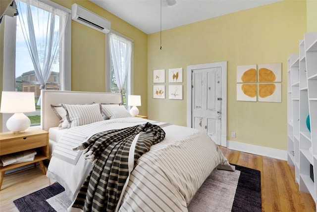 bedroom featuring baseboards, wood finished floors, and an AC wall unit