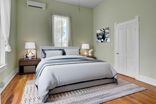 bedroom with an AC wall unit, baseboards, and wood finished floors