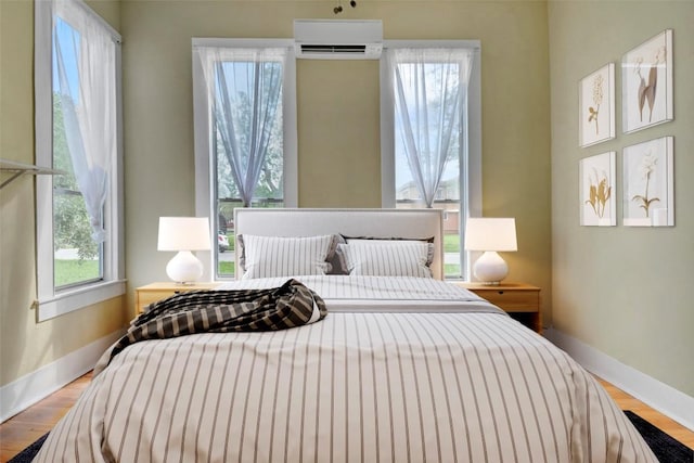 bedroom with baseboards, a wall mounted AC, and wood finished floors
