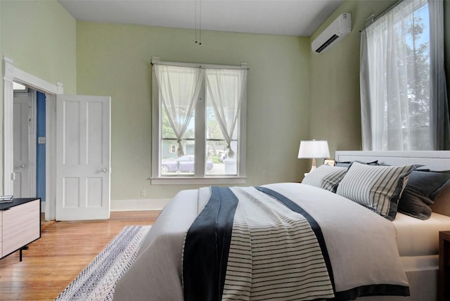 bedroom with baseboards, a wall mounted AC, and wood finished floors
