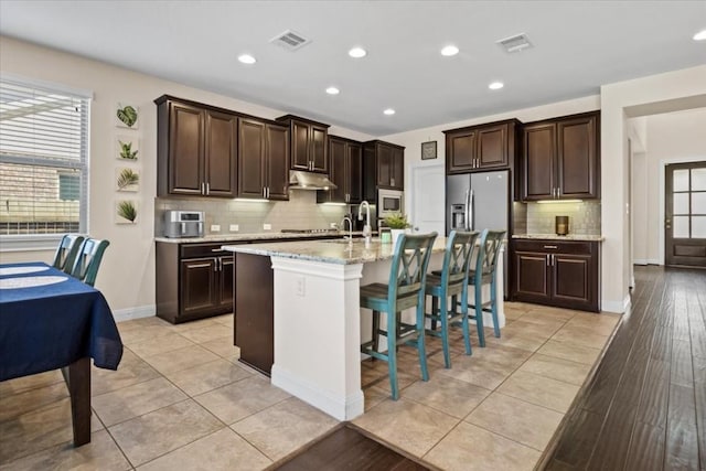 2316 Centennial Loop, Round Rock, TX 78665 - kitchen featuring under cabinet range hood, decorative backsplash, a kitchen bar, dark brown cabinets, and recessed lighting
