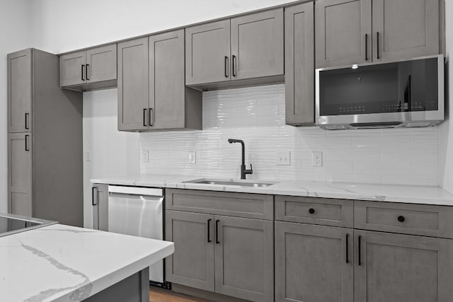 2450 Wickersham Ln Unit 2021, Austin, TX 78741 - kitchen with stainless steel appliances, a sink, backsplash, light stone counters, and gray cabinetry