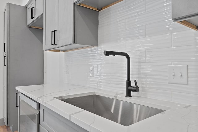 2450 Wickersham Ln Unit 2021, Austin, TX 78741 - kitchen view of a sink, backsplash, light stone countertops, and gray cabinetry