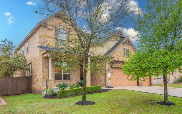 view of front of home with stone siding, concrete driveway, fence, and a front lawn