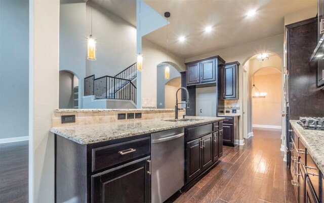 kitchen featuring stainless steel dishwasher, backsplash, a sink, arched walkways, and dark wood-style floors