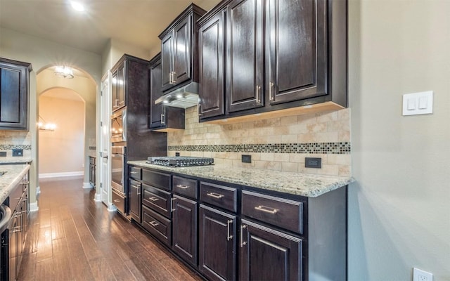 kitchen with gas stovetop, under cabinet range hood, decorative backsplash, arched walkways, and dark wood-style floors