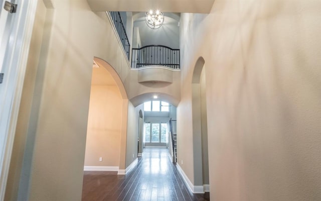 corridor featuring dark wood-style floors, a high ceiling, arched walkways, and baseboards