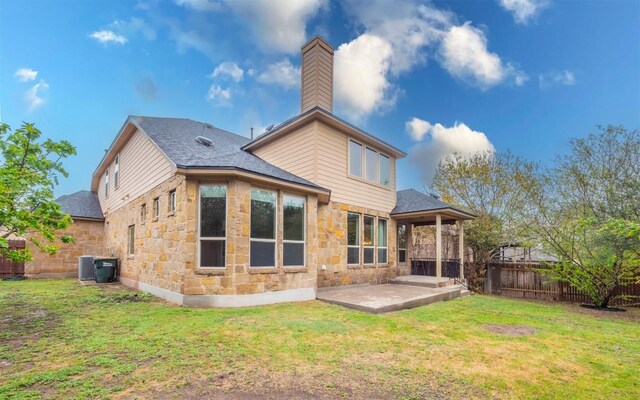 back of house with fence, a lawn, a patio area, and stone siding