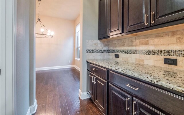 kitchen with a notable chandelier, dark brown cabinetry, light stone countertops, dark wood finished floors, and decorative backsplash