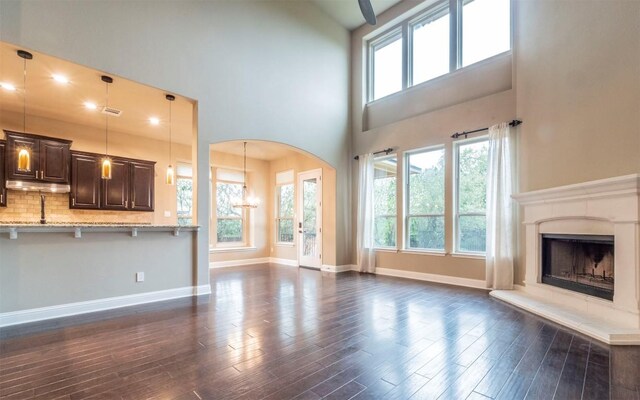 unfurnished living room with plenty of natural light, arched walkways, a premium fireplace, and dark wood-style flooring