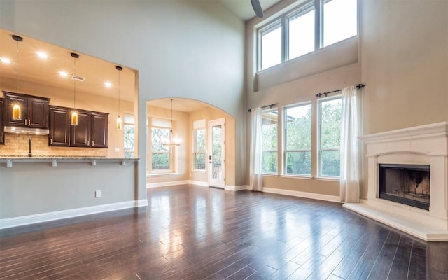 296 Elderberry Rd, Austin, TX 78737 - unfurnished living room featuring dark wood-style floors, arched walkways, a fireplace, a high ceiling, and baseboards