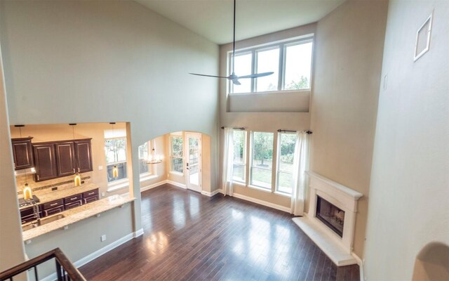 living room with dark wood finished floors, baseboards, a fireplace with raised hearth, and a towering ceiling