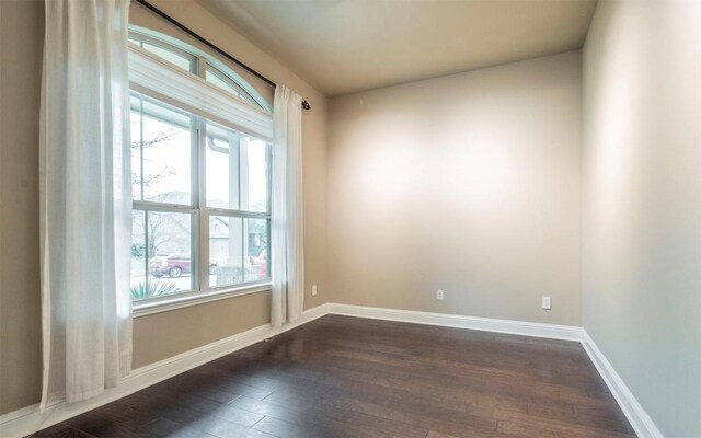 spare room with baseboards and dark wood-style flooring