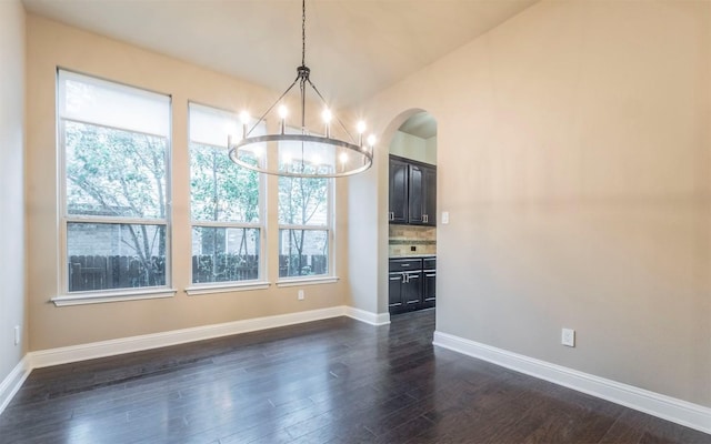 unfurnished dining area with arched walkways, baseboards, a chandelier, and dark wood finished floors