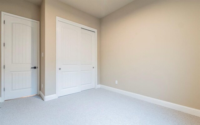 unfurnished bedroom featuring light carpet, baseboards, and a closet