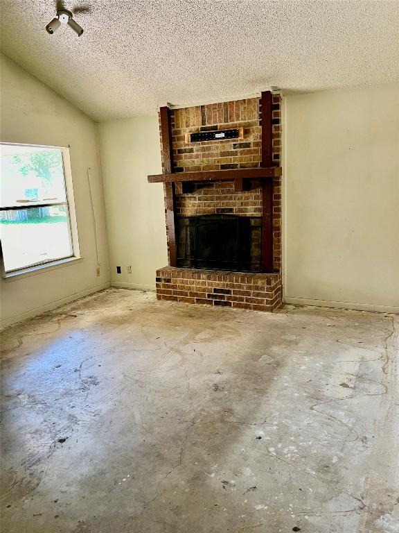 313 Golden Oaks Dr, Georgetown, TX 78628 - unfurnished living room featuring a textured ceiling, a brick fireplace, and concrete floors