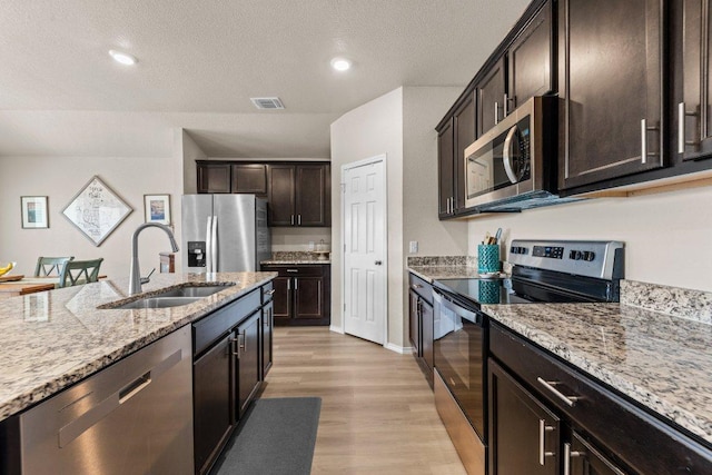 8517 Cantera Ridge Rd, Temple, TX 76502 - kitchen featuring stainless steel appliances, a sink, light wood finished floors, light stone counters, and dark brown cabinetry