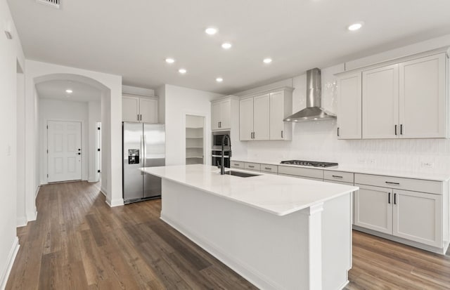 417 Singing Dove Way, Liberty Hill, TX 78642 - kitchen featuring stainless steel appliances, wall chimney exhaust hood, arched walkways, a center island with sink, and dark wood-style floors