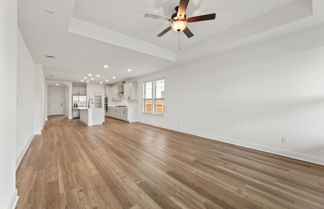 417 Singing Dove Way, Liberty Hill, TX 78642 - unfurnished living room featuring a raised ceiling, light wood-style flooring, arched walkways, a ceiling fan, and recessed lighting