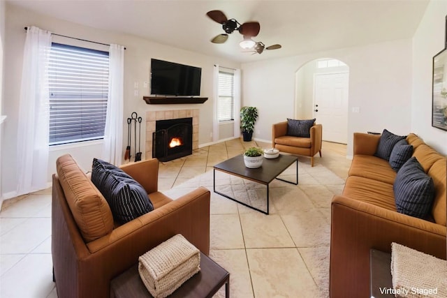 115 Hummingbird Ct, Cedar Creek, TX 78612 - living room with light tile patterned floors, a ceiling fan, a tiled fireplace, arched walkways, and baseboards