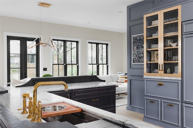 901 Wayside Dr, Austin, TX 78703 - kitchen featuring glass insert cabinets, light stone countertops, a sink, and hanging light fixtures