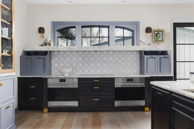 901 Wayside Dr, Austin, TX 78703 - kitchen featuring oven, light wood-style flooring, tasteful backsplash, dark cabinetry, and light stone counters
