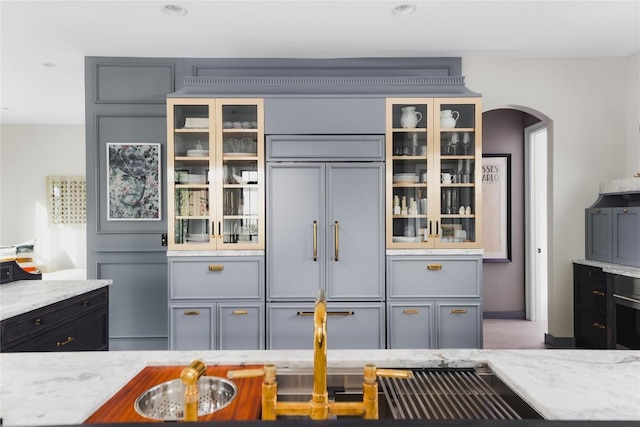 901 Wayside Dr, Austin, TX 78703 - kitchen featuring paneled refrigerator, light stone countertops, arched walkways, and glass insert cabinets
