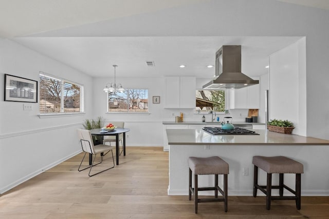 11305 Songbird Cv, Austin, TX 78750 - kitchen with island exhaust hood, stainless steel gas cooktop, white cabinets, a chandelier, and light wood-style floors