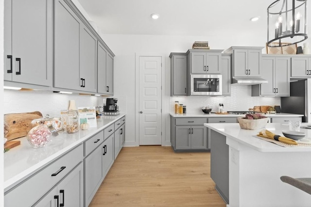 100 Silent Grove Ct, Georgetown, TX 78642 - kitchen featuring stainless steel microwave, gray cabinetry, under cabinet range hood, backsplash, and light wood-style flooring