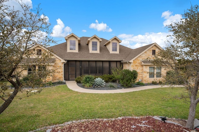 view of front of house featuring stone siding, a sunroom, roof with shingles, and a front lawn