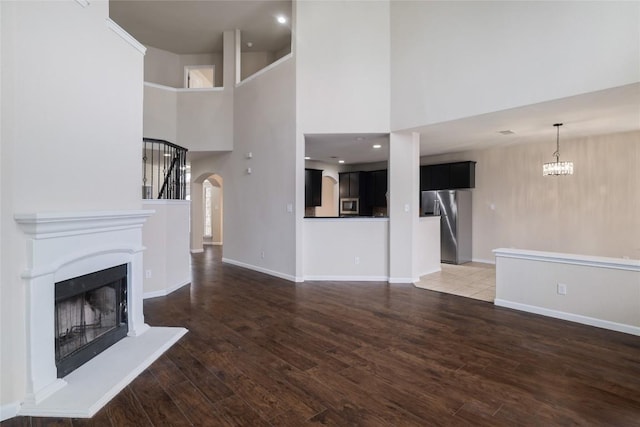 19803 Mallard Pond Trl, Pflugerville, TX 78660 - unfurnished living room with arched walkways, a high ceiling, wood finished floors, and a fireplace with raised hearth