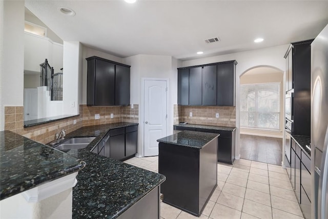 19803 Mallard Pond Trl, Pflugerville, TX 78660 - kitchen featuring arched walkways, dark stone countertops, tasteful backsplash, light tile patterned flooring, and stainless steel appliances