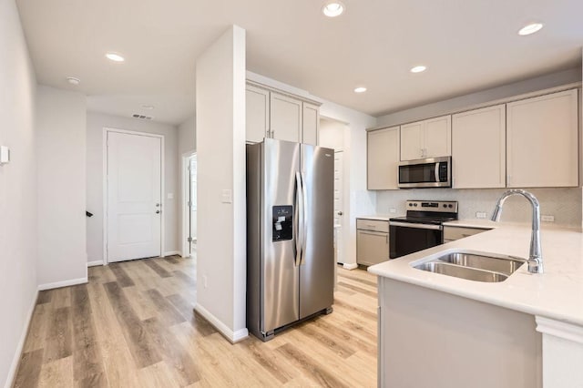 kitchen with light countertops, a sink, backsplash, light wood finished floors, and appliances with stainless steel finishes