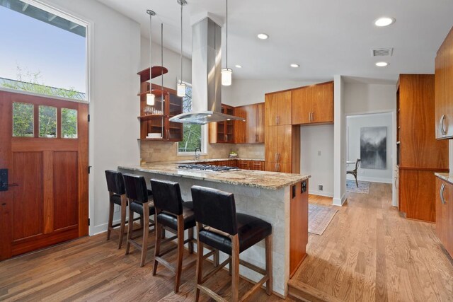 2300 S 3rd St, Austin, TX 78704 - kitchen with island range hood, brown cabinetry, a peninsula, light stone countertops, and light wood-type flooring